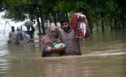Displaced people wade through a flooded area in Peshawar, Khyber Pakhtunkhwa. Since June, nearly 900 people have died by severe monsoon rains and floods in Pakistan, while thousands have been displaced and millions more affected. Thousands of people who live in areas under threat of flooding have been told to evacuate. Photo by Hussain Ali/Anadolu Agency via Getty Images