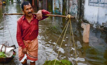 An Indian vegetable vendor carries his wares through floodwaters in Siliguri, West Bengal, on July 24, 2016. AFP/Diptendu Dutta 2016.