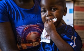 Tatiana* holding Arka* as he eats Ready-to-Use Therapeutic Food