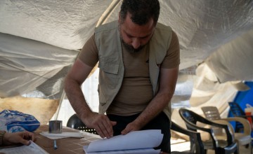 Manar*, an aid worker, distributes cash support to beneficiaries at a camp in Jenderis, Syria. As part of our DEC funded response to the Syria-Turkey earthquakes, cash assistance is distributed to displaced families living in camps and temporary shelters to meet their immediate basic needs. After an informational session, each household receives a cash voucher at the distribution point. Credit: Arete