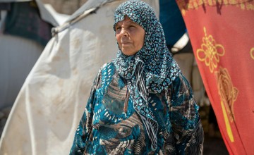 Shahinaz* poses for a photograph next to her tent at a camp in northwest Syria. As part of DEC funded response to the Syria-Turkey earthquakes, cash assistance is distributed to displaced families living in camps and temporary shelters to meet their immediate basic needs