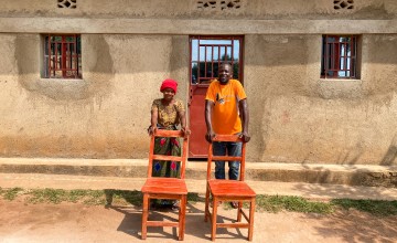 Joel and Charlotte outside the house they built, along with two wooden chairs that Joel made.