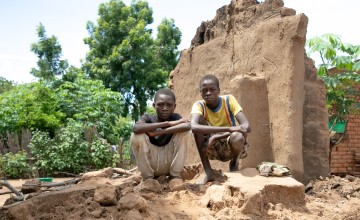 Brothers, Charity(16) and Fraction (14) standing on what's left of their home. Their home was washed away with all their belongings. The brothers family are casual labourers. With no crops to harvest, his parent won't have any work this season. Location: