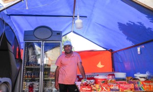 A man stands in the middle of his grocery shop, which is being housed in a temporary tent