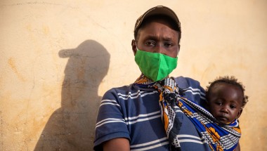 A woman in a mask holds her baby and looks at the camera defiantly