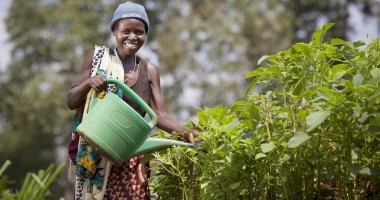 A woman stands in a vegetable garden holding a watering can