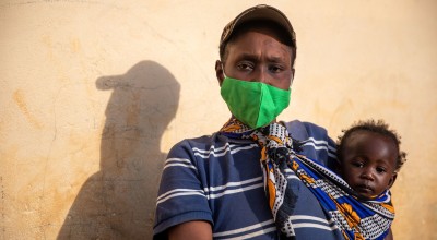A woman in a mask holds her baby and looks at the camera defiantly